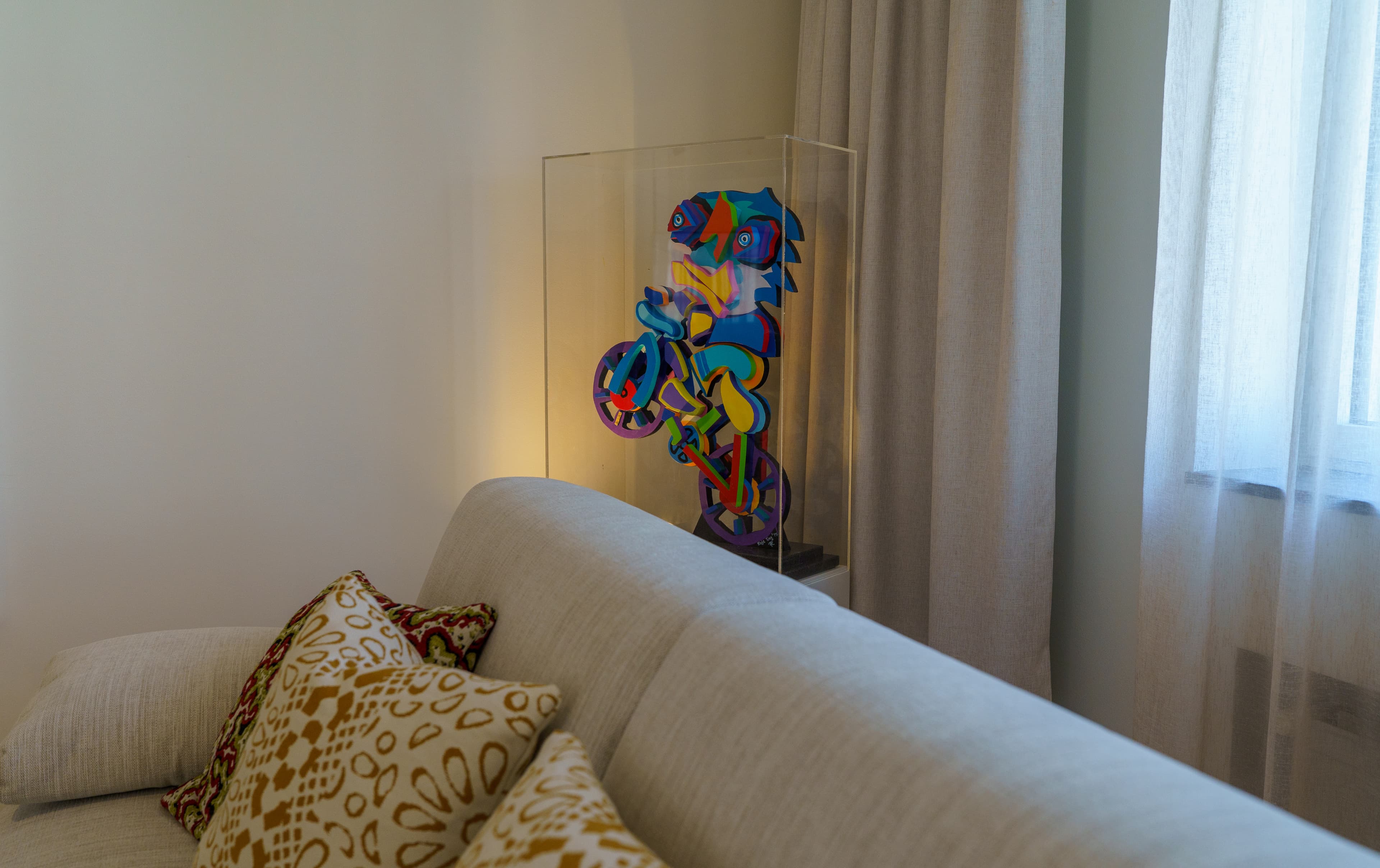 Colorful cyclist sculpture on display behind a linen sofa in a light-filled room