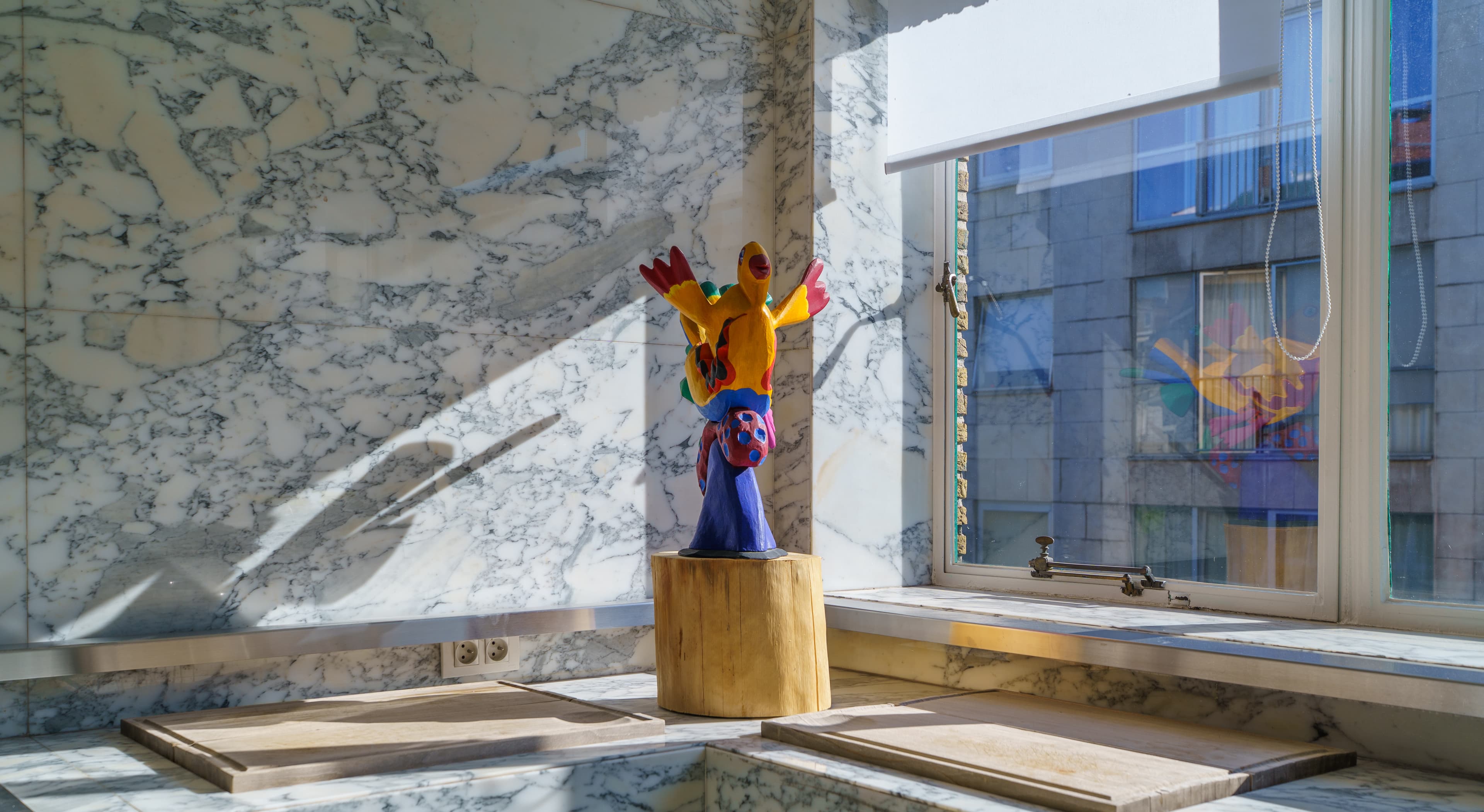 Vivid figurative sculpture on a wooden plinth against a marble wall