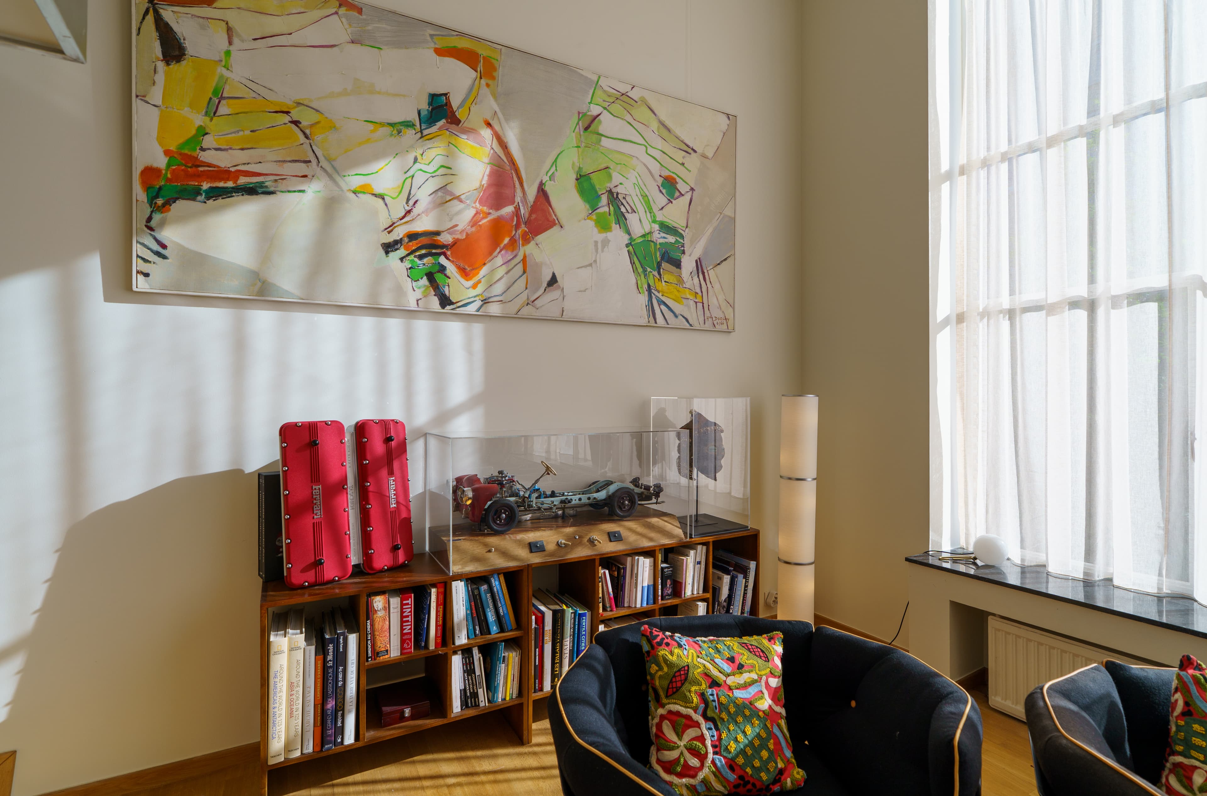 Large abstract painting above book-lined shelves, with sculptures and a velvet armchair