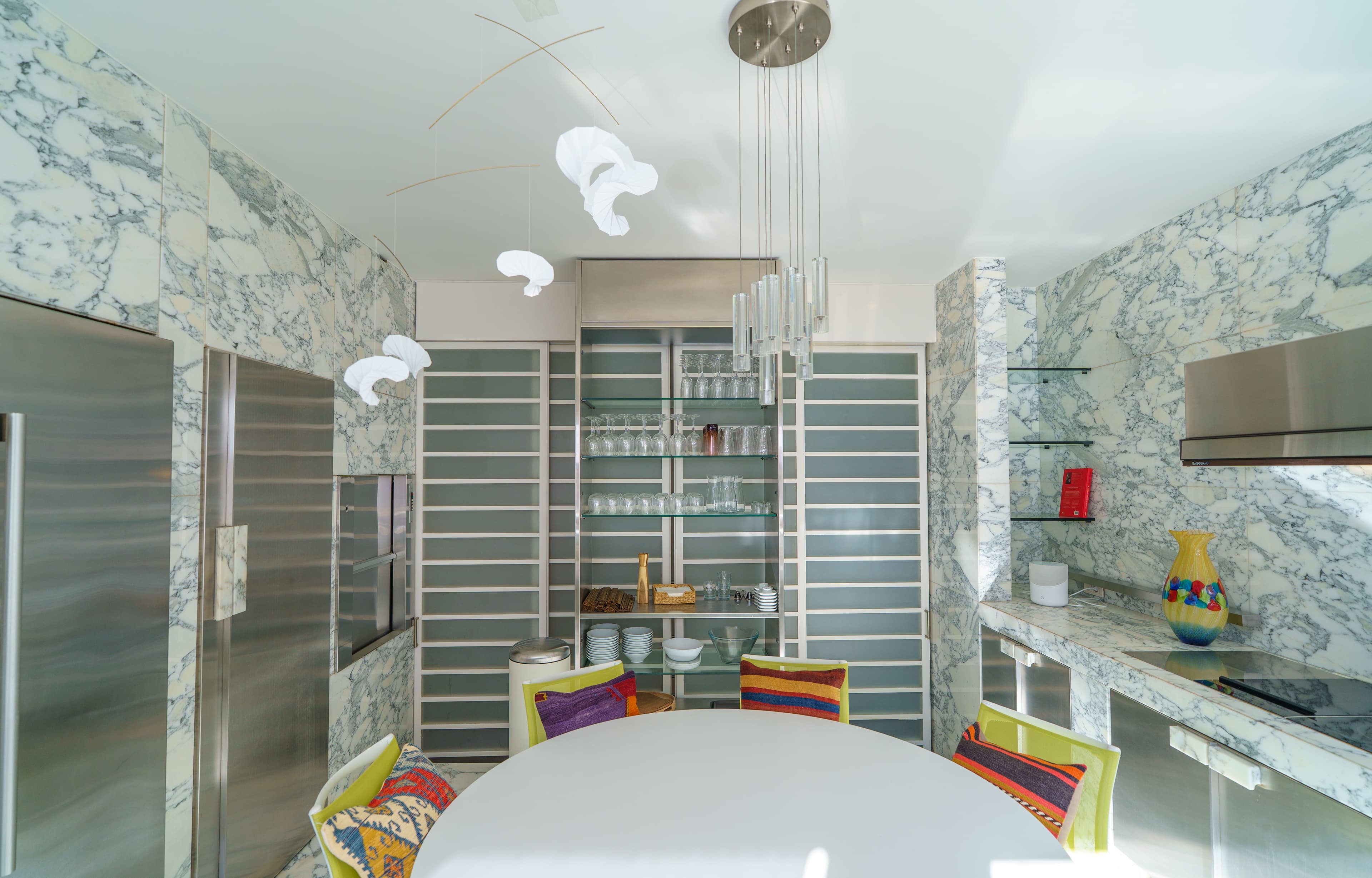 Marble kitchen with a wall of glassware shelving and pendant lights