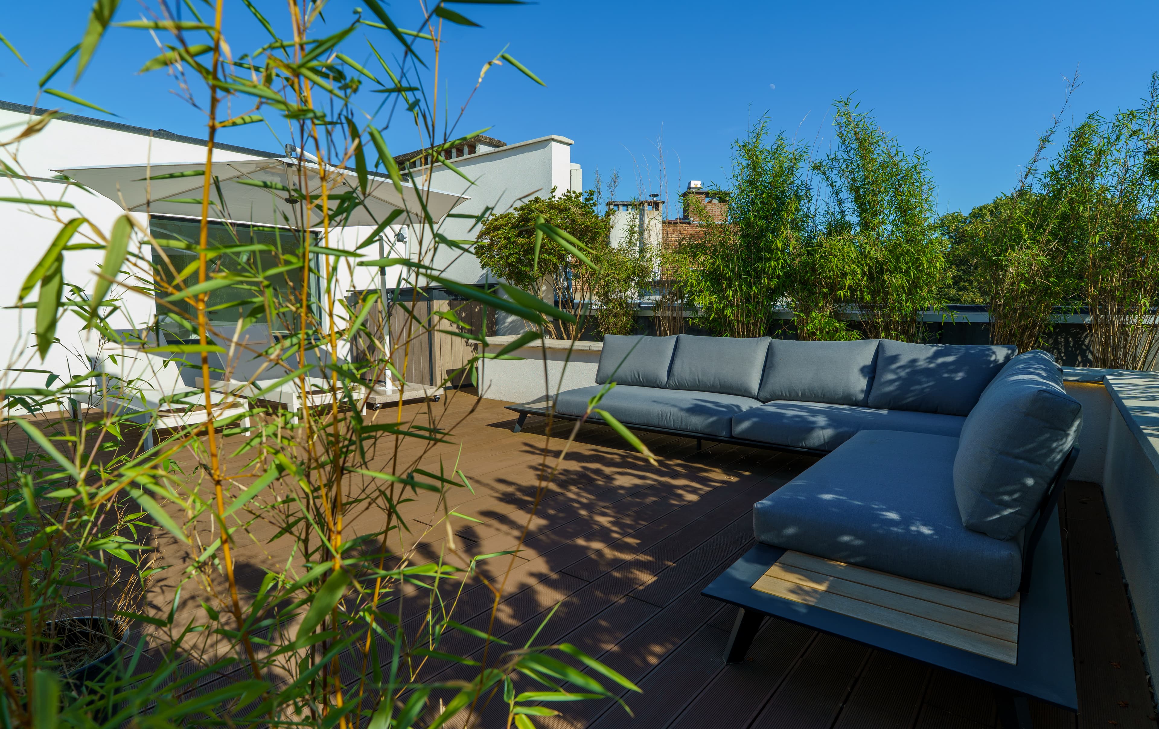 Outdoor lounge sofa on the rooftop terrace, screened by bamboo under a blue sky